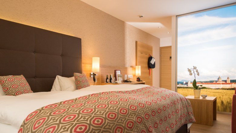 Modernes Hotelzimmer mit Doppelbett, stilvollen Lampen und gro&szlig;em Fenster mit Landschaftsansicht.