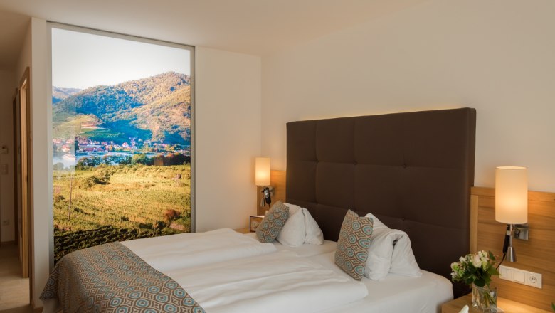 Modernes Hotelzimmer mit Doppelbett, dekorativen Kissen und gro&szlig;em Landschaftsbild an der Wand.