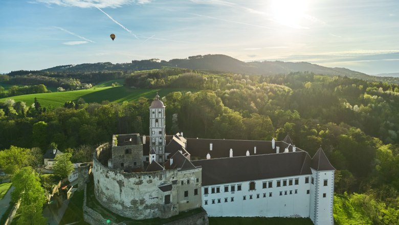 Luftaufnahme der Schallaburg mit umliegender Landschaft und einem Hei&szlig;luftballon am Himmel.