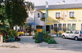Ein gelbes Gebäude mit der Aufschrift 'Gasthof-Pension Zur Hammerschmiede'. Vor dem Gebäude stehen Tische, Stühle und ein Auto.