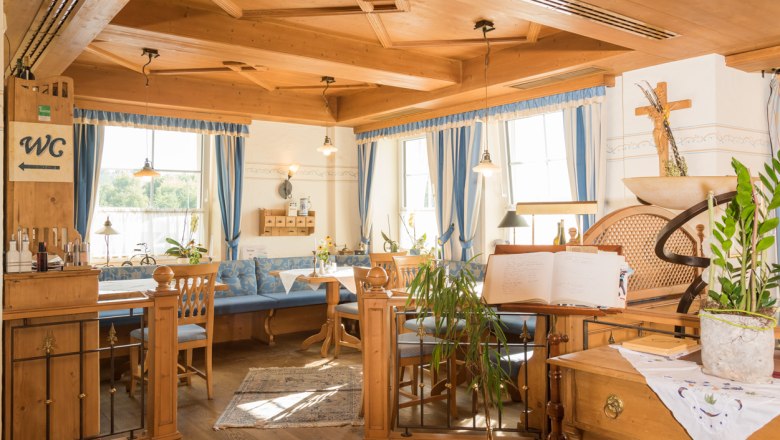 Gem&uuml;tlicher Restaurantbereich mit Holzm&ouml;beln und blauen Vorh&auml;ngen.