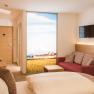 Modernes Hotelzimmer mit Doppelbett, rotem Sofa, Flachbildfernseher und gro&szlig;em Fenster mit Landschaftsausblick.