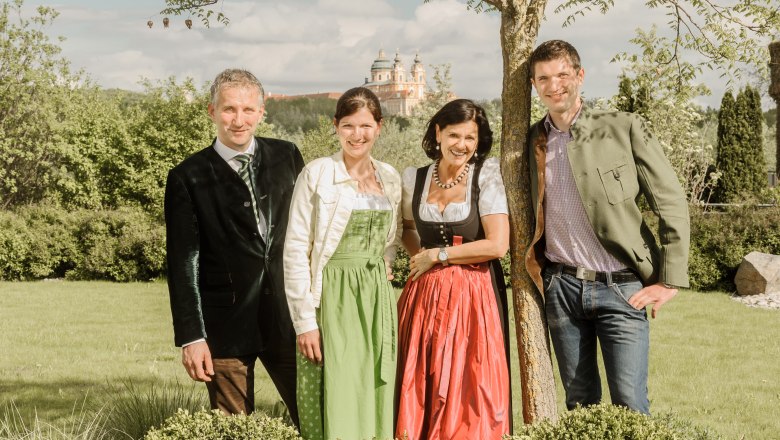 Familie Pichler  in traditioneller Kleidung stehen im Freien vor einem Baum, im Hintergrund ist Sift Melk zu sehen